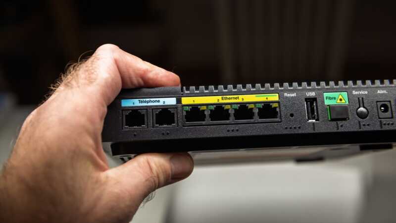 Un homme tient une box internet par la main et on voit l'arrière de l'appareil