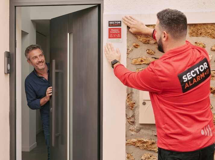 Un technicien en uniforme installe une plaque de sécurité sur le mur près d'une porte d'entrée avec un homme.