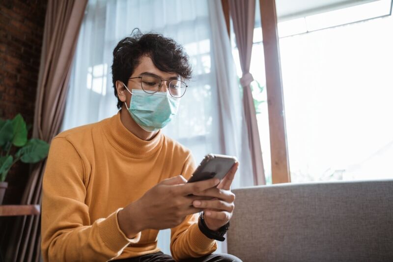 Un jeune homme masqué consulte son téléphone mobile pendant le confinement