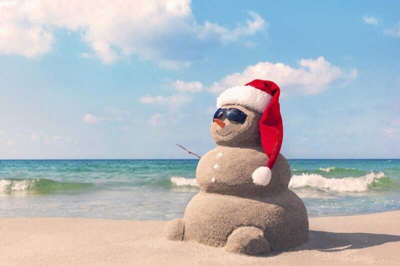 Un bohomme de neige avec un bonnet de Noël sur une plage
