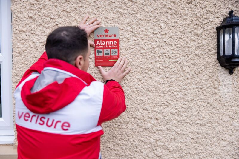 Un technicien Verisure installe une plaque "Alarme Verisure" sur le mur d'une maison